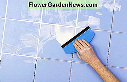 Anvend hvide fuglblanding til en mur med blĂĄ fliser. Applying white grout mix to a wall with blue tiles.